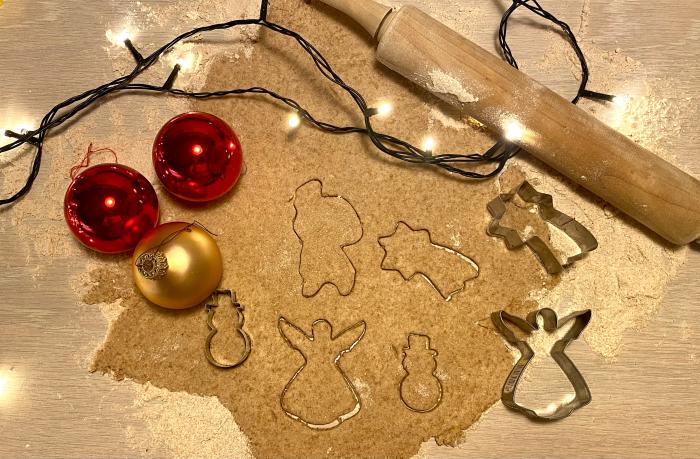 Der Salzteig wurde ausgerollt und schon mehrere weihnachtliche Plätzchen ausgestochen. Daneben liegen Weihnachtskugeln und eine Lichterkette. 