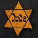 Schwarzer Hintergrund. Darauf ein gelber Judenstern mit der Aufschrift in altdeutscher Schrift "Jude"