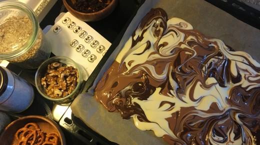 Gemischte Schokolade auf Backblech; Toppings stehen am Rand: Walnüsse, Kokos, Rosinen, Zuckeraugen, Salzbrezeln