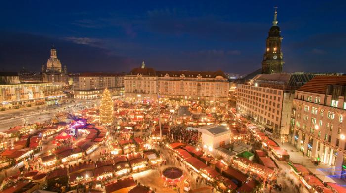 der Striezelmarkt in Dreseden von oben (Weihnachtsmarkt auf dem Altmarkt), im Hintergrund Häuser und eine Kirche, auf dem Marktplatz unzählige Buden und Stände, alles mit tausenden von Lichtern hell erleuchtet
