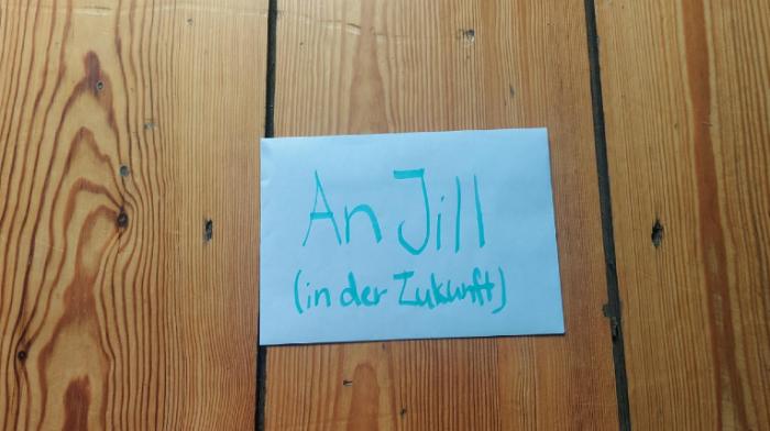 auf einem hölzernen Hintergrund kann man einen weißen Brief im Umschlag sehen. Auf dem Umschlag steht "Für Jill (in der Zukunft)