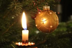 Zu sehen ist ein geschmückter Weihnachtsbaum mit einer brennenden Kerze und einer goldenen Weihnachtsbaumkugel.