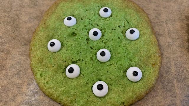 Zu sehen ist die Nahaufnahme eines grünen Kekses mit Zuckeraugen.
